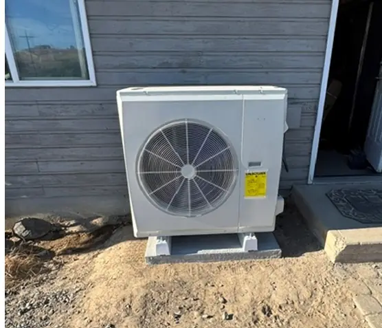 Heat pump condenser on a block pad against grey siding