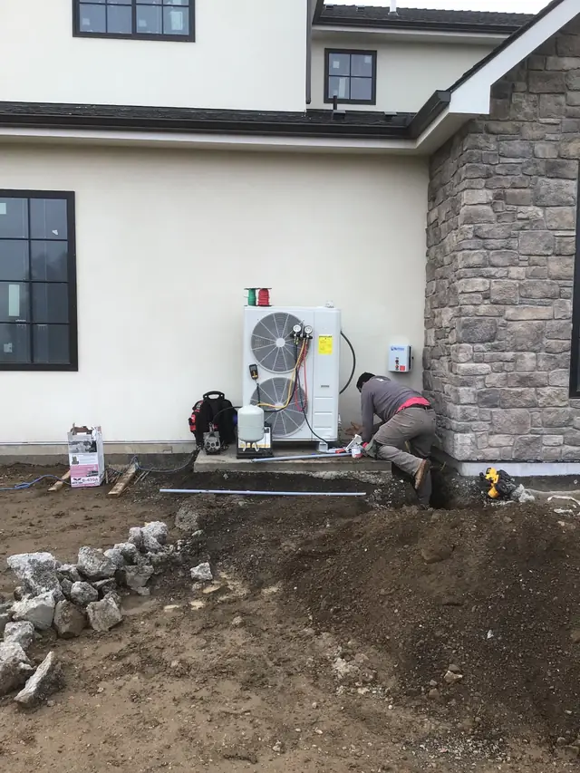 A Paul's AIR FX technician tying in a new twin-fan heat pump beside a stone wall
